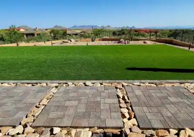 “Modern desert-style backyard featuring artificial turf, concrete pavers, and rip rap stone designed and installed by Eclipse Landscape & Design in Scottsdale, AZ.”